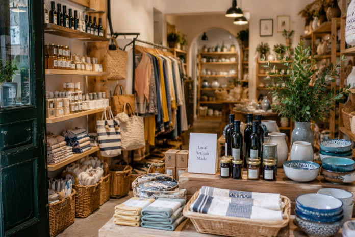 Kleine unabhängige Boutique in einer südeuropäischen Altstadt mit handgefertigter Keramik, Textilien, Lederwaren und regionalen Produkten, natürliches Tageslicht und authentische Reiseatmosphäre.