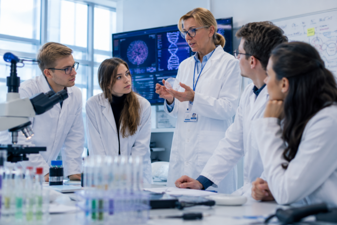Eine Wissenschaftlerin erklärt einer Gruppe von Studierenden moderne Forschungsergebnisse in einem hellen Labor mit digitalen Bildschirmen.