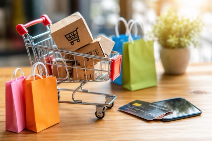 Person bestellt mit einem Laptop und Smartphone in einem modernen Wohnzimmer online ein Paket.
